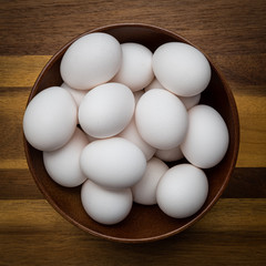 Fresh white eggs in a brown bowl on a wood countertop