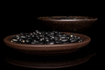 Lot of whole black bean in glazed bowl with brown ceramic coaster isolated on black glass