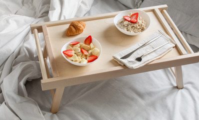 European breakfast in bed: oatmeal, banana, strawberry,  croissant. Copy space. Horizontal...