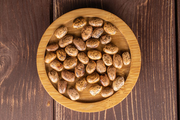 Lot of whole mottled brown bean pinto on round bamboo coaster flatlay on brown wood