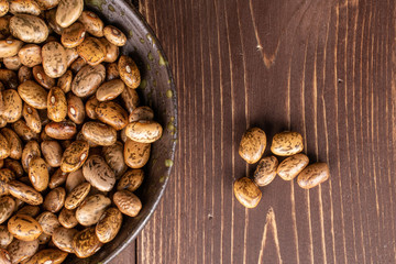 Lot of whole mottled brown bean pinto in glazed bowl flatlay on brown wood