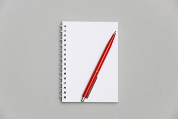 Blank notebook or notepad with red pen on gray desk background. 
