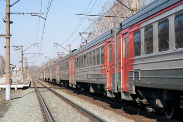 Russian electric train in red, orange, gray. Railway, poles with wires. Spring day