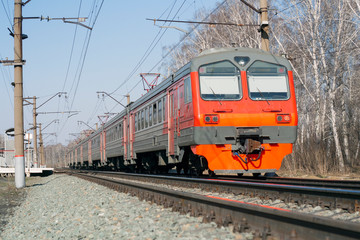 Fototapeta na wymiar Bright beautiful Russian electric train of red, orange, gray. Railroad, posts with wires