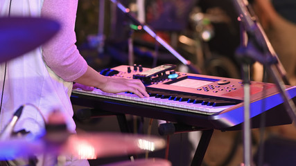 Closeup night musician working as electrical pianist while sitting and playing at his electric piano with the blurred night stage as background.