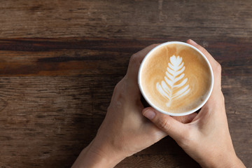 Topviews of hands holding Late coffee cup on old wooden table background