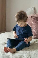 Boy sitting with a tablet in the room. The boy lies on a bed and plays on the tablet.