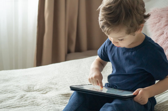Boy sitting with a tablet in the room. The boy lies on a bed and plays on the tablet.