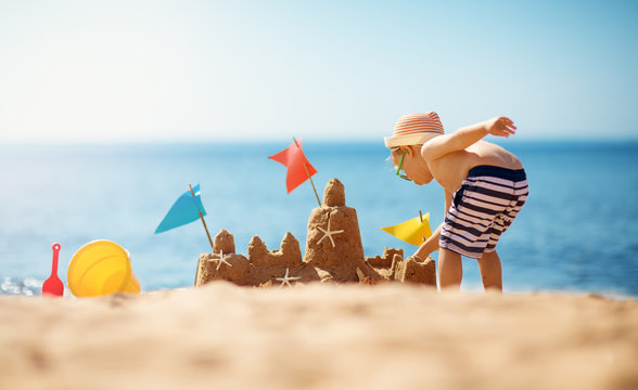 boy building a sandcastle at the beach in summer