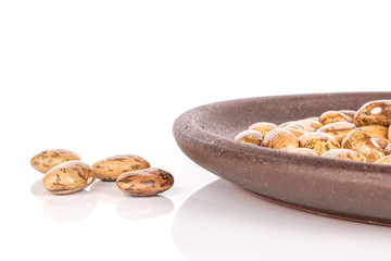 Lot of whole mottled brown bean pinto with brown ceramic coaster isolated on white background