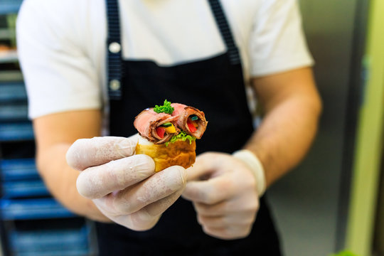 Man hands holding piece of bruschetti with meat and vegetables.