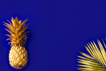View from above. Golden, glamorous pineapple fruit on a dark blue background, shaded with golden palm leaves. place for text or postcard.  Copy Space