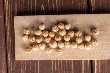 Lot of whole fresh tan chickpea on wooden cutting board flatlay on brown wood