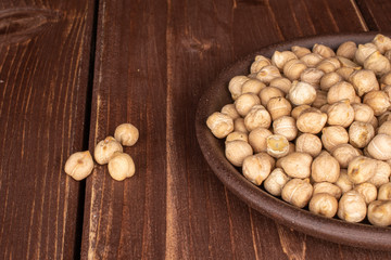 Lot of whole fresh tan chickpea with brown ceramic coaster on brown wood