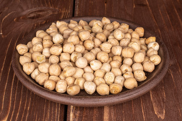 Lot of whole fresh tan chickpea with brown ceramic coaster on brown wood