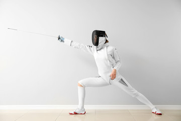 Young female fencer against white wall