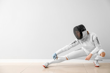Young female fencer against white wall