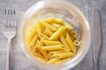 Nieugotowany makaron penne na stole w słoiku, obok sztućce