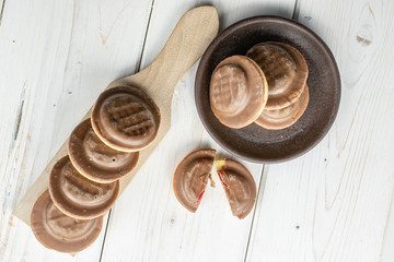 Group of seven whole two halves of chocolate biscuit with brown ceramic coaster on wooden cutting board flatlay on white wood