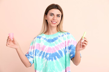Young woman with menstrual cup and tampon on color background
