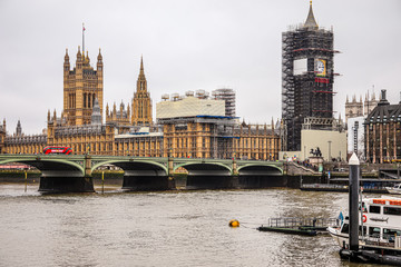 Big Ben iconic clock tower in London under construction. Famous British landmark, House of Parliament in a cloudy day, double-decker bus and people on the Westminster Bridge around Thames River in UK