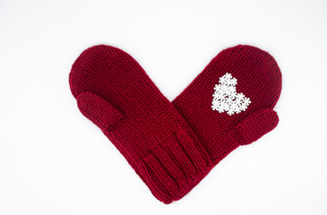 A knitted red mittens with white snowflakes in the shape of a heart on a white background, isolated. Concept of Christmas, winter, love. Care and Valentine's day. Copy space