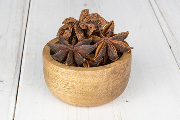 Lot of whole aromatic brown badian in bamboo bowl on white wood