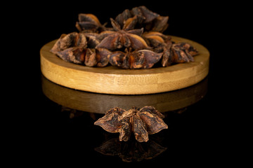 Lot of whole aromatic brown badian on round bamboo coaster isolated on black glass