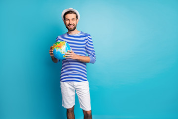 Photo of attractive funky guy holding big world globe map choosing where to travel vacation wear striped sailor shirt shorts panama pants isolated blue color background