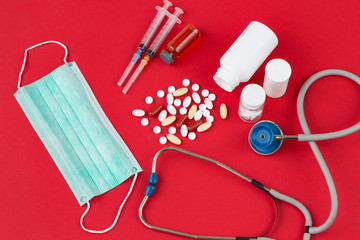 on a red background a stethoscope, pills, two syringes, a mask 