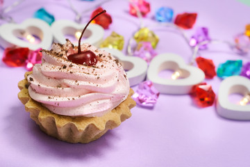 cake with pink cream and cherry on a purple background.garland of hearts.multicolored glass stones