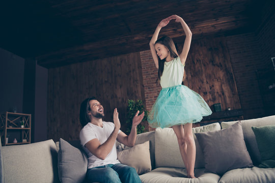 Photo of little energetic pretty lady excited handsome daddy watching daughter school dance raise hands like ballerina sitting sofa clapping arms ovation house room indoors