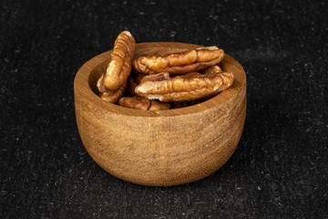 Lot of whole tasty brown pecan half in bamboo bowl on grey stone