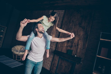 Photo of little funky beautiful lady sitting on shoulders excited handsome daddy carry daughter playing games hold hands cheerful good mood rejoicing house room indoors