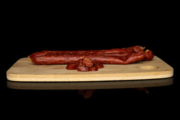 Group of two whole lot of slices of piquant smoked sausage on bamboo cutting board isolated on black glass