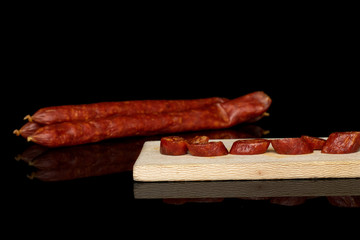 Group of three whole five slices of piquant smoked sausage on wooden cutting board isolated on black glass