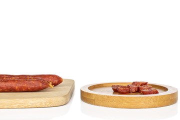 Group of three whole lot of slices of piquant smoked sausage on bamboo cutting board on round bamboo coaster isolated on white background