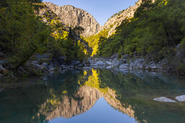 Fototapeta na wymiar Beautiful green mountains of canyon reflected in mirror surface of rocky lake or river. Horizontal photography of peaceful scenic landscape of Turkey.