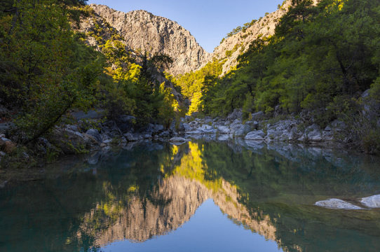 Beautiful green mountains of canyon reflected in mirror surface of rocky lake or river. Horizontal photography of peaceful scenic landscape of Turkey.