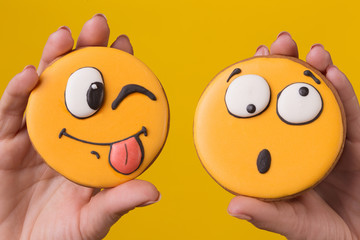 two female hands are holding two gingerbread cookies in the form of funny emoticons with different emotions, concept
