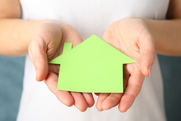 Woman holding paper house against blue background, close up