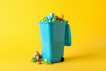 Recycle bin with trash on yellow background, space for text