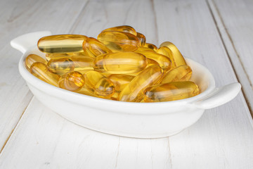 Lot of whole golden fish oil on white ceramic plate on white wood
