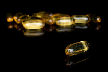 Lot of whole disordered golden fish oil isolated on black glass