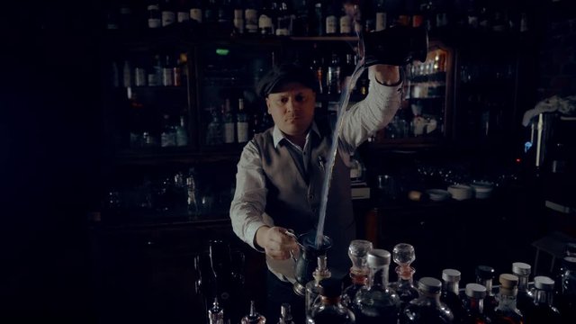 The bartender is preparing a punch or grog in a speakeasy style bar.  Jet of burning drink, camera movement.