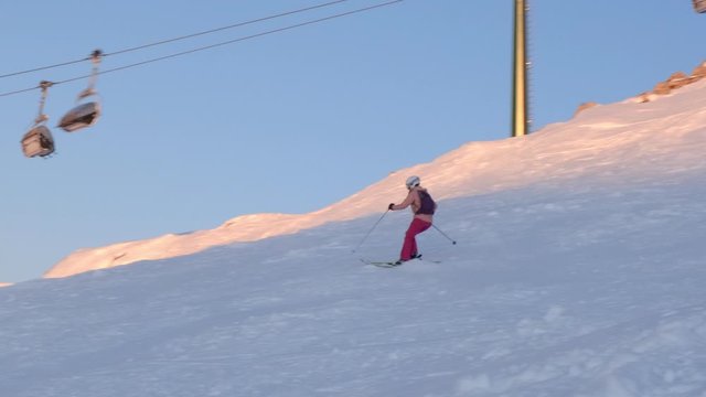 Woman skis off-piste at sunset, near a chairlift, at Dolomiti Superski domain in Italy, next to a ski slope.