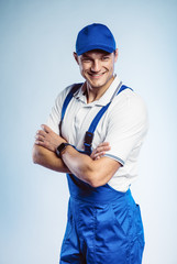 Portrait of young worker man wearing blue uniform with crossing hands. Isolated on grey background with copy space. Human face expression, emotion. Business concept.