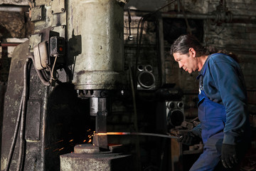 blacksmith processes a hot workpiece with a machine hammer