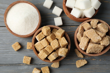 Bowls with different sugar on wooden background, top view