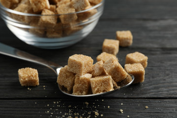 Bowl and spoon with brown sugar on wooden background, close up